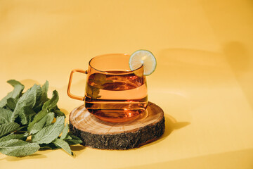 Mint tea in a glass orange mug on a wooden stand on a yellow background with a shadow. Front view