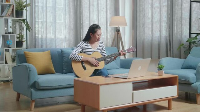 Asian Woman Having Video Call On Laptop And Playing A Guitar At Home

