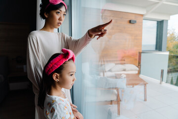 Fototapeta na wymiar Asian woman and her daughter looking out window while together
