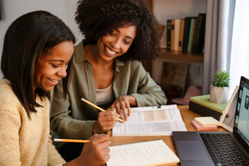 Black girl writing in exercise book while doing homework with her mother