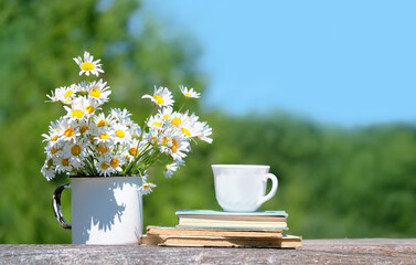 tea cup, bouquet of daisies and book on table in garden, natural background. picnic, relax, harmony mood. romantic summer seasonal still life.
