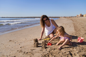 a girl making sand castles on the beach with a mother