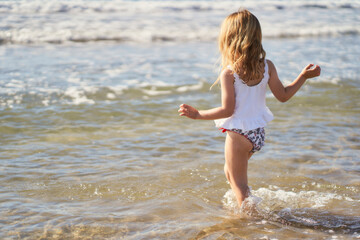Little girl on the beach walking towards the water