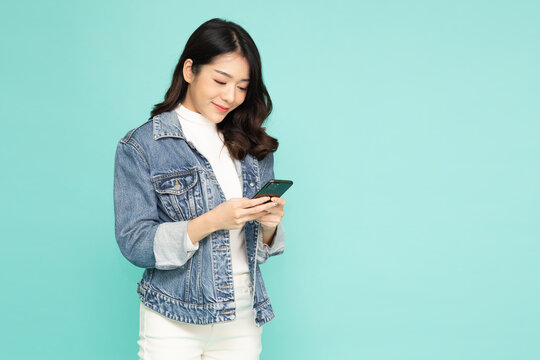 Happy young Asian woman using mobile phone or touching screen application on smartphone isolated on green background