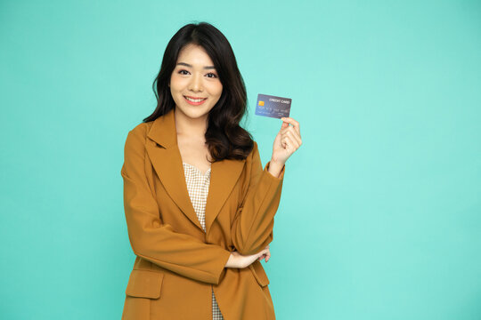 Happy young Asian business woman smiling and showing credit card for paying online business isolated on green background