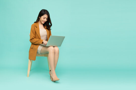 Happy young Asian business woman using laptop computer and sitting on chair isolated on green background