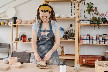 Young woman in workwear tying wrapped and packed earthenware item prepared for client with thread while standing by workplace