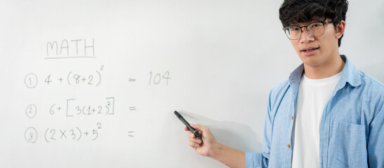 Male tutor standing in front of whiteboard and writing math equations on board to explaining new lesson