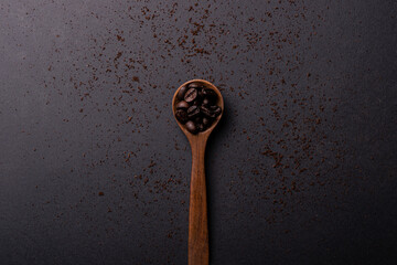 Scattered ground coffee accompanied by a spoon full of coffee beans, located in the center. Top view plane.