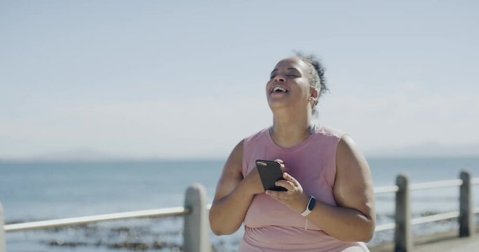 One young plus size woman celebrating a weight loss journey and focusing on health, cardio, fitness, and energy. Happy woman getting fit with a run and speed walking app on her phone at the beach