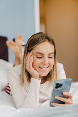 Young white blond woman smiling and using cellphone in bed at home