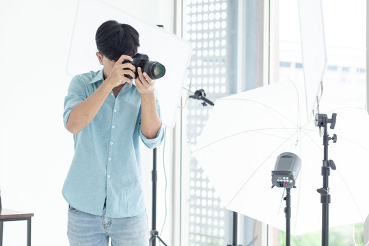 An Asian male photographer standing and shooting in his studio. With studio lights as a backdrop and copy space.