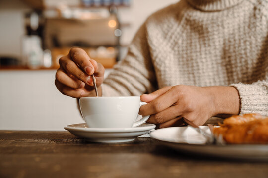 Man stiring coffee sitting at cafe with croissant cropped close-up