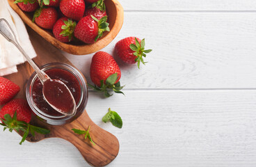 Strawberry jam. Strawberry jam in glass jar with fresh berries plate on white wooden table background, closeup. Homemade strawberry fruity jam. Top view with copy space.