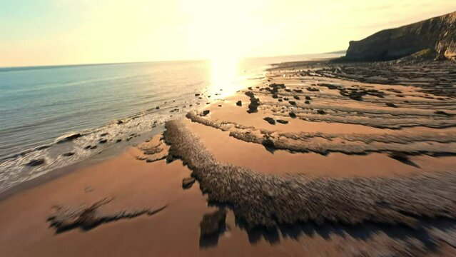 4K FPV Aerial view of monk nash beach known as the jurassic coast, stunning fast flying low across golden sandy beach with cliff side on the right.