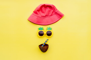Top view funny face made of pink bucket hat, pineapple shape sunglasses and cocktail in coconut...