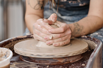 Hands of young creative female artisan holding by rotating pottery wheel while producing new earthenware items for sale in workshop