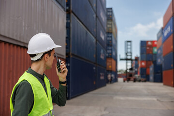 the caucasian engineer using walky talky comunicate with lifting container team with blue sky....