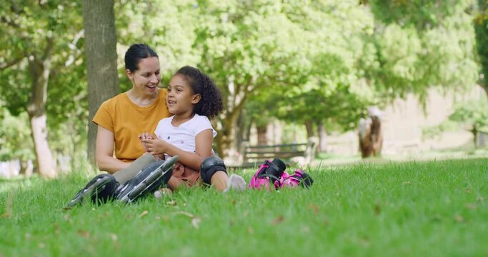 Happy mother and her cute adopted daughter relaxing and talking on the grass in a public park on a sunny day. Smiling woman and little daughter bonding and sharing an affectionate kiss in a garden