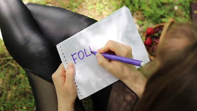 Faithful Christian woman writing the quote "Follow God" on a blank notebook page with a marker while sitting in nature. Obey God Jesus Christ, biblical concept. A closeup.