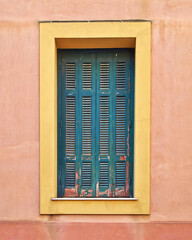 A window with green shutters on orange walls.