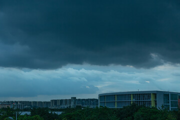 The sky was layered with thick clouds piled up in the sky. The buildings and trees under the clouds...