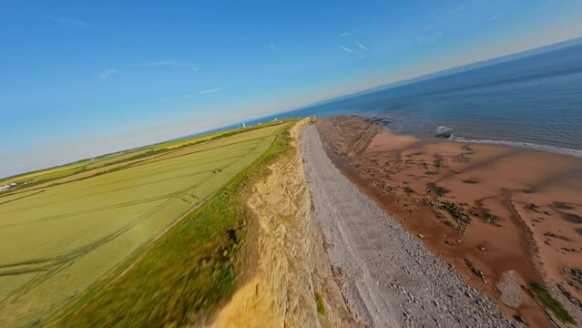 4K FPV Aerial view of monk nash beach known as the jurassic coast, stunning fast flying low across golden sandy beach with cliff side on the right.