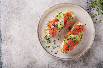 Sandwiches. Salmon toast with cream cheese, cucumber, black sesame and microgreens on gray concrete table background. Seafood. Healthy food. Top view.