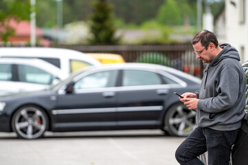 Fototapeta na wymiar man with smartphone standing next to the car, using mobile app for paying, car lock or Internet