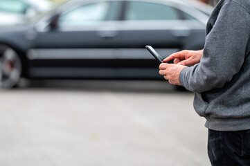 man with smartphone standing next to the car, using mobile app for paying, car lock  or Internet