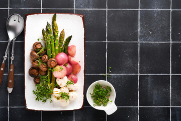 Asparagus, mushrooms, mozzarella cheese, grilled radish and cress salad, oil olive salad on rectangular ceramic plate on black old tile table background. Healthy diet grilled food concept. Top view.