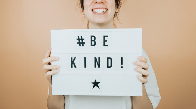 Young woman smiling to camera while holding a sign hastag( be kind ) with positive vibes to camera. Cheering people concept.help and self help concept, mental health. color background with copy space.