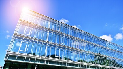 Fototapeta premium Blue sky reflection in glass facade of building. View of office building windows close up with sunrise, reflection and perspective..Bright sunny day with sunbeams on the blue sky.Velvia graphic filter