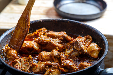 Chicken pieces stewed in pad thai sauce in spices in a deep frying pan with a wooden spatula.