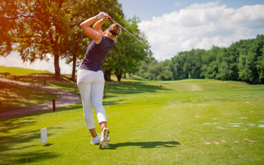 Sporty woman golfer player doing golf swing tee off on the green evening time, she presumably does...