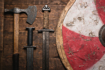 Old battle swords, axe and shield on the wooden table background top view.