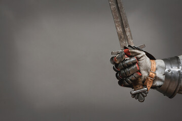 Sword in knight hand isolated on the gray background close up.