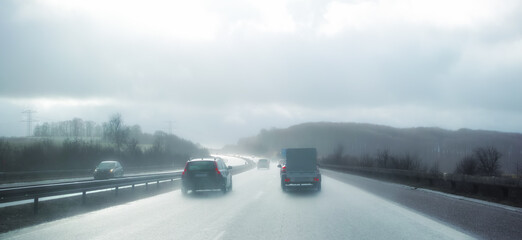 Cars at breaking distance on a highway on a rainy day in Denmark. Motor vehicles driving on a...
