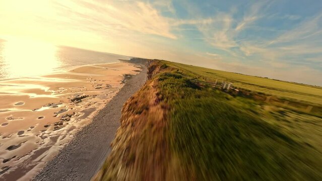 4K FPV Aerial view of monk nash beach known as the jurassic coast, stunning fast flying low across golden sandy beach with cliff side on the right.