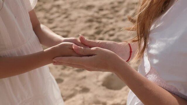 Mother and daughter, both in white dresses holding hands. Ocean scene.