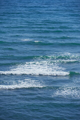 Calm waves in the empty ocean on a sunny day. Beautiful sea water with light ripple effects on the surface. Abstract aqua textures in the deep wide sea. White foam patterns in the Atlantic or pacific