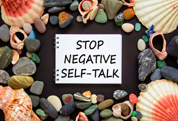 Stop negative self-talk symbol. Concept words Stop negative self-talk on a beautiful black background. Sea stones and seashells. Psychological and stop negative self-talk concept. Copy space.