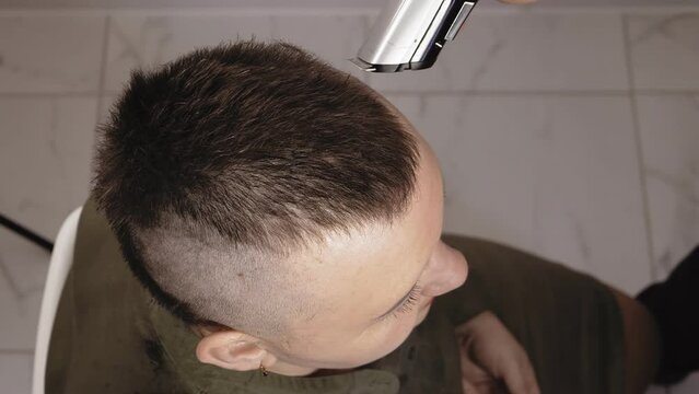 A man barber shaves a woman with a machine leaving a mohawk