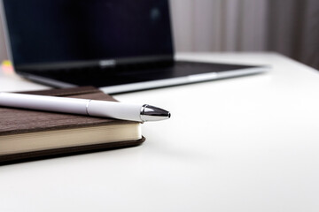 White office desk with notebook, pen and laptop. Selective focus.