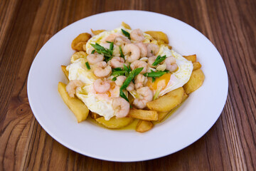 plate with fried eggs, french fries, garlic sprouts and grilled prawns