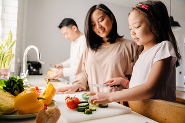 Happy asian family with little daughter cooking together in kitchen