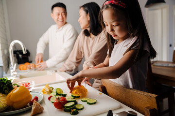 Happy asian family with little daughter cooking together in kitchen