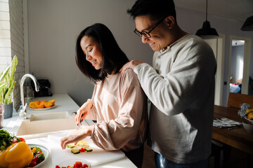 Happy asian man and woman smiling and cooking in kitchen at home