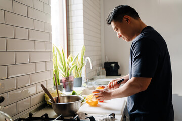 Adult asian man cutting vegetables and cooking in cozy kitchen