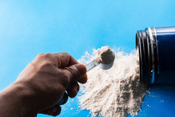 A person's hands holding a scoop full of dietary supplement powder.